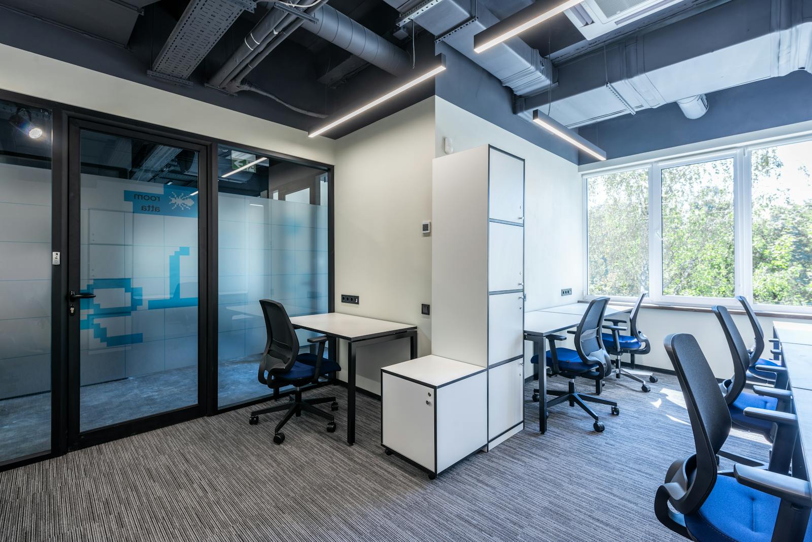 Desks with armchairs placed in spacious open space office with glass doors and white cupboards near big window in business center